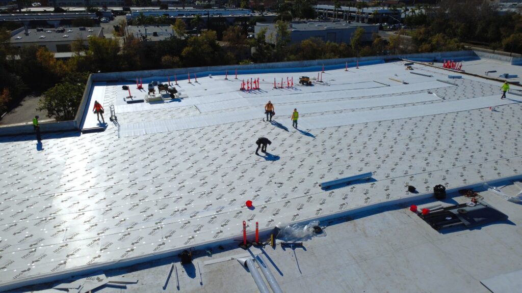 Roofers installing white membrane on roof