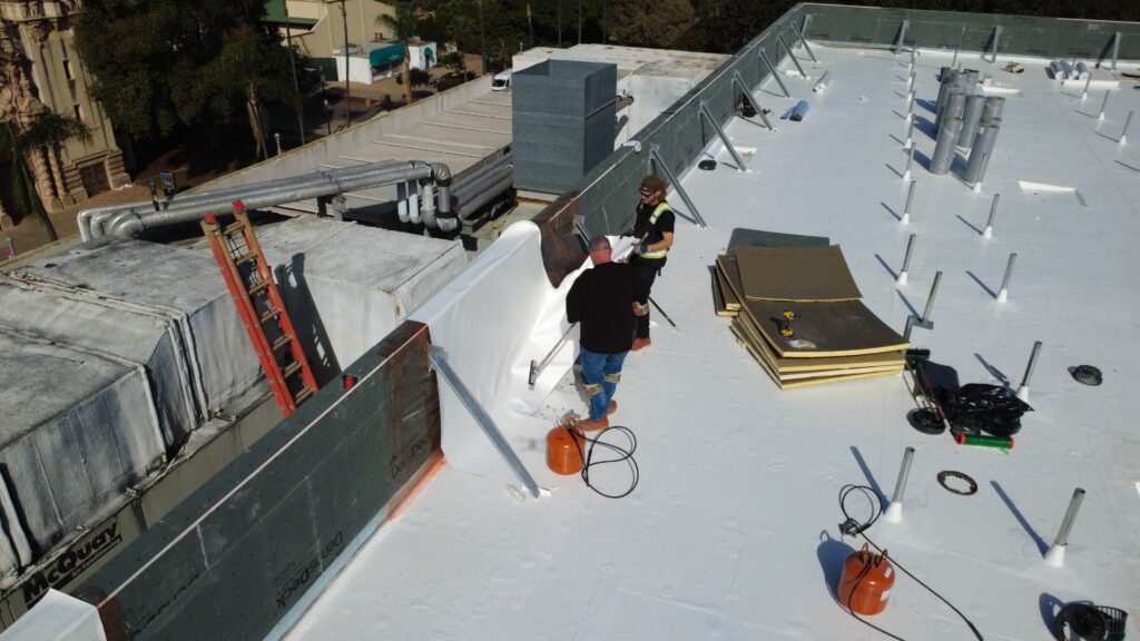 Roofers installing white membrane near ductwork