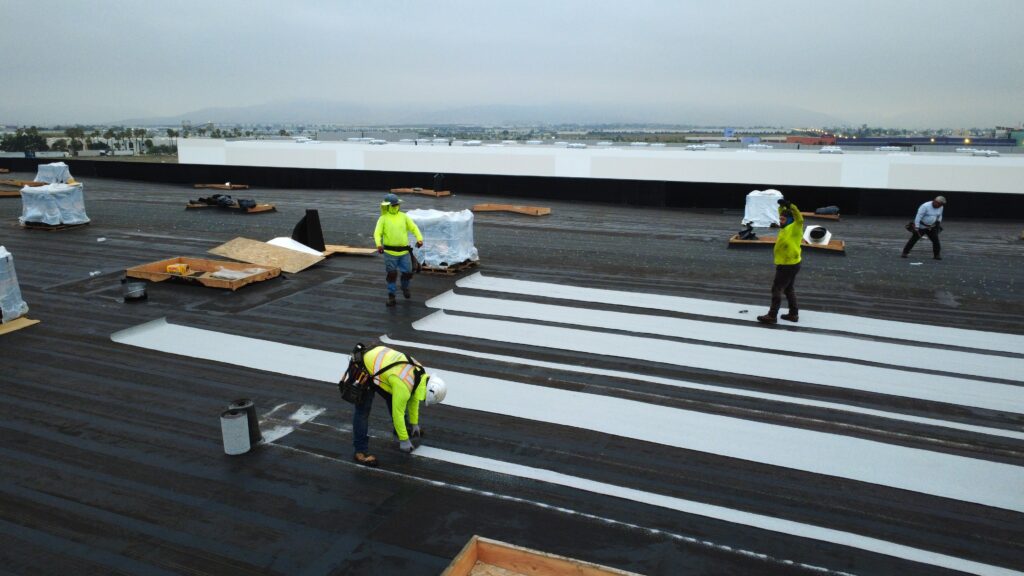 Crew applying white roofing strips on membrane